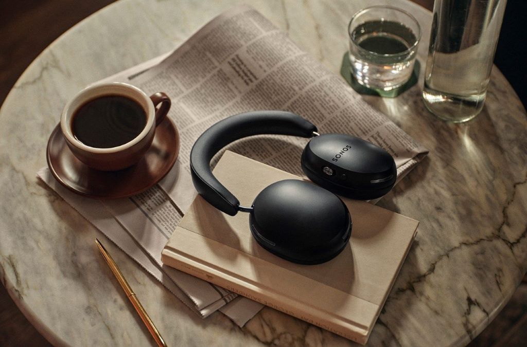 A pair of sleek, black wireless travel headphones folded neatly next to their carrying case on a wooden table