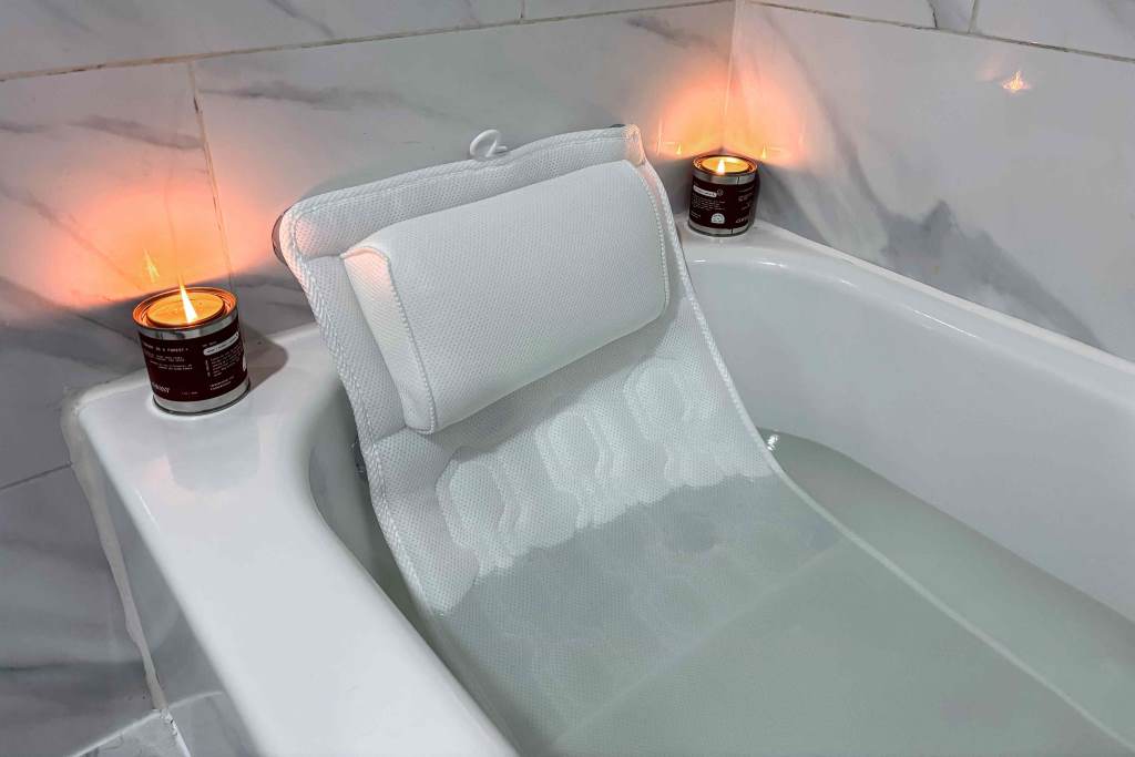 Person reading a book propped on a wedge bath pillow in a modern bathtub.