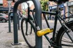 Heavy-duty yellow U-lock securing a city bicycle to a metal rack.